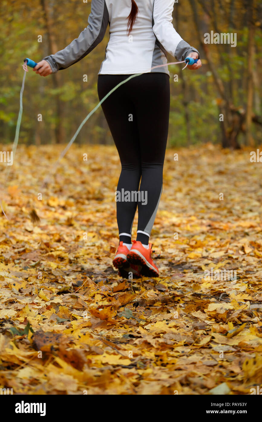 Photo de l'arrière du sports girl in sneakers sautant avec la corde à sauter à la forêt d'automne, le matin Banque D'Images