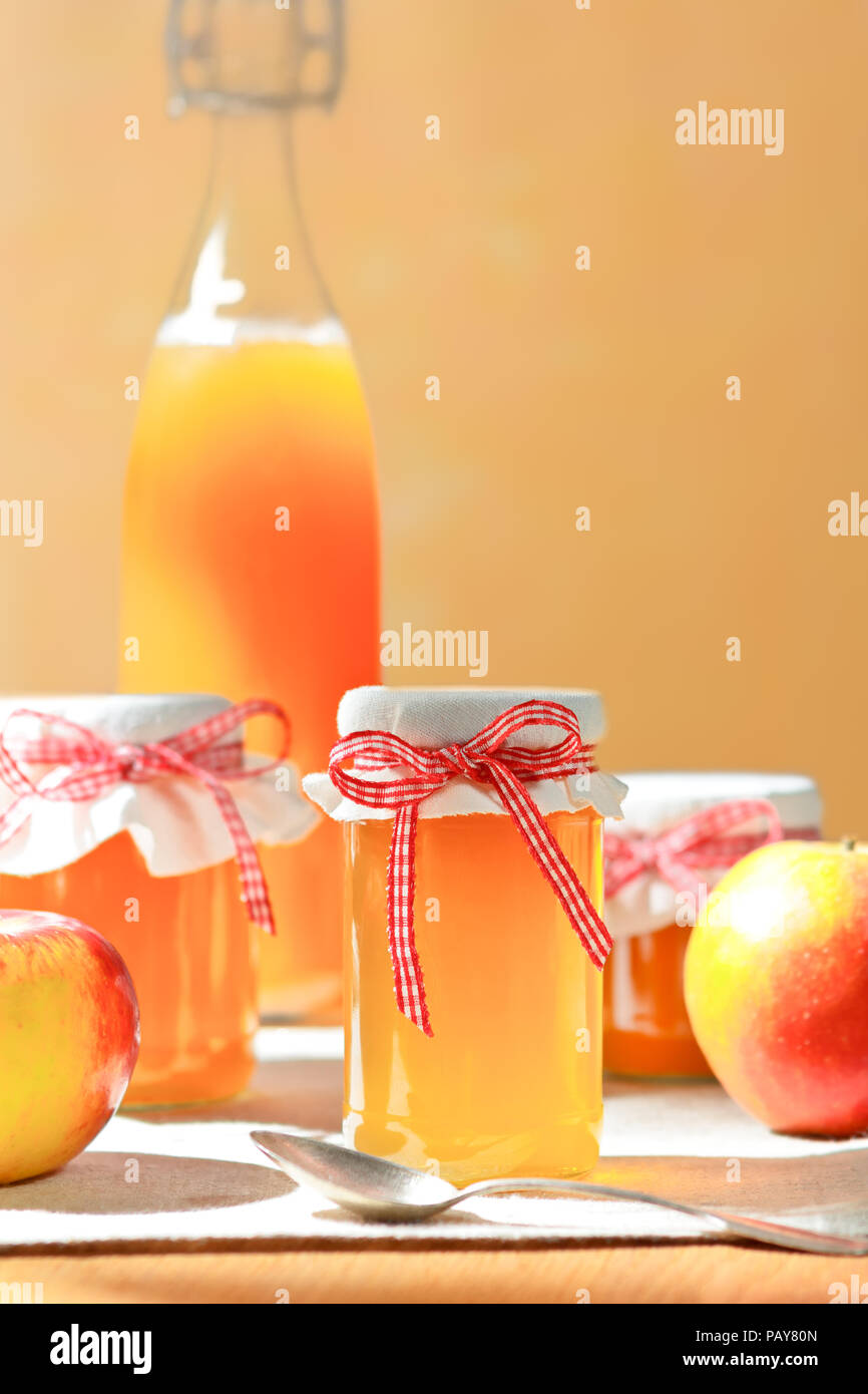 Jus de pommes maison dans une bouteille en verre et la gelée dans les pots avec lin et un nostalgique ribbon bow en plein soleil devant un fond de couleur abricot. Banque D'Images