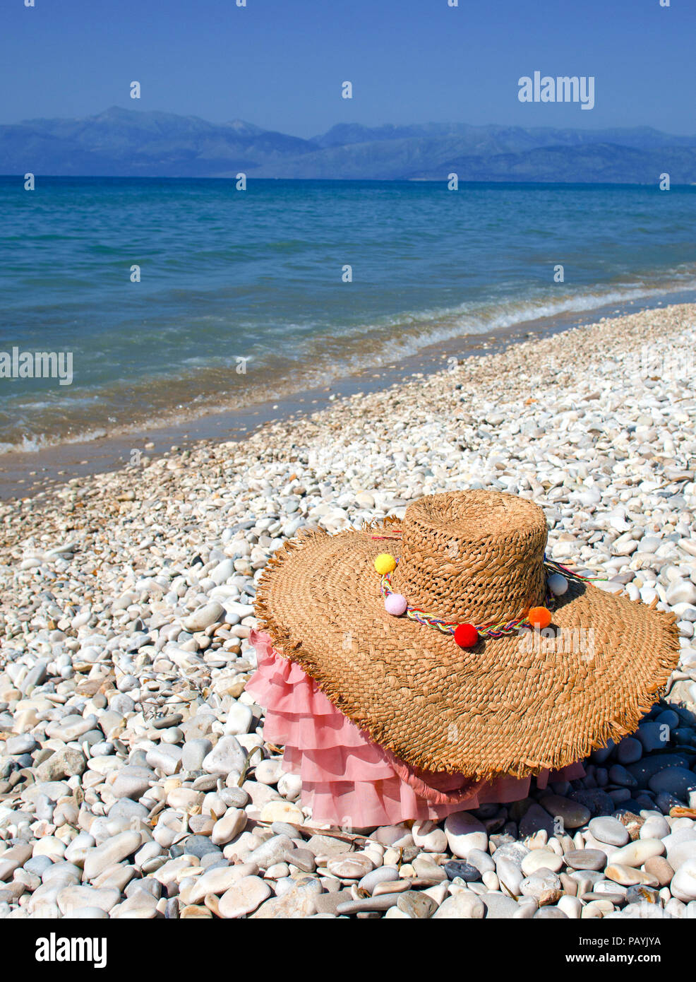 Chapeau et sac sur une plage de galets à Corfou avec l'Albanie en arrière-plan. Banque D'Images