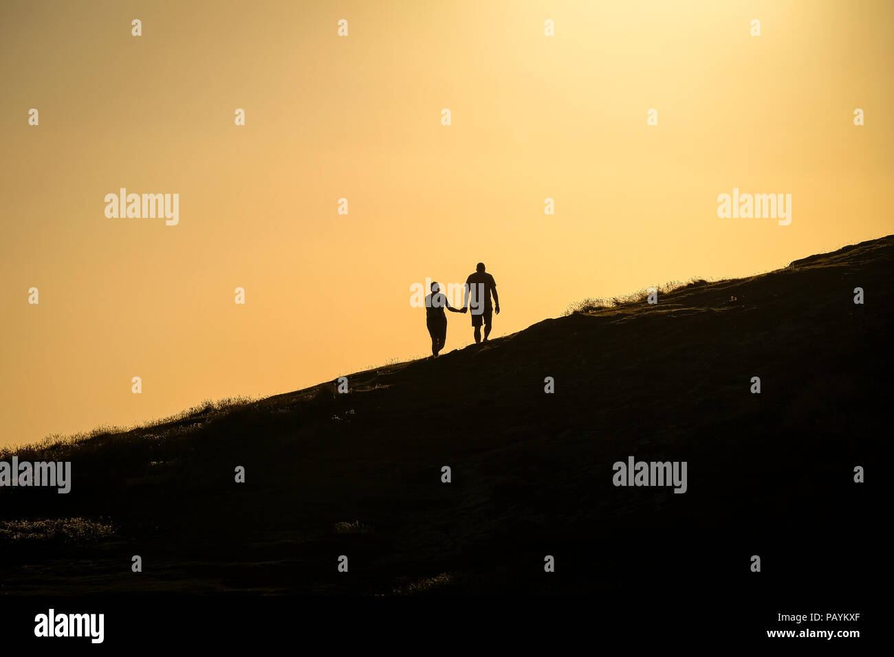 Un couple holding hands à marcher vers le sommet d'une colline pour admirer le coucher du soleil Banque D'Images