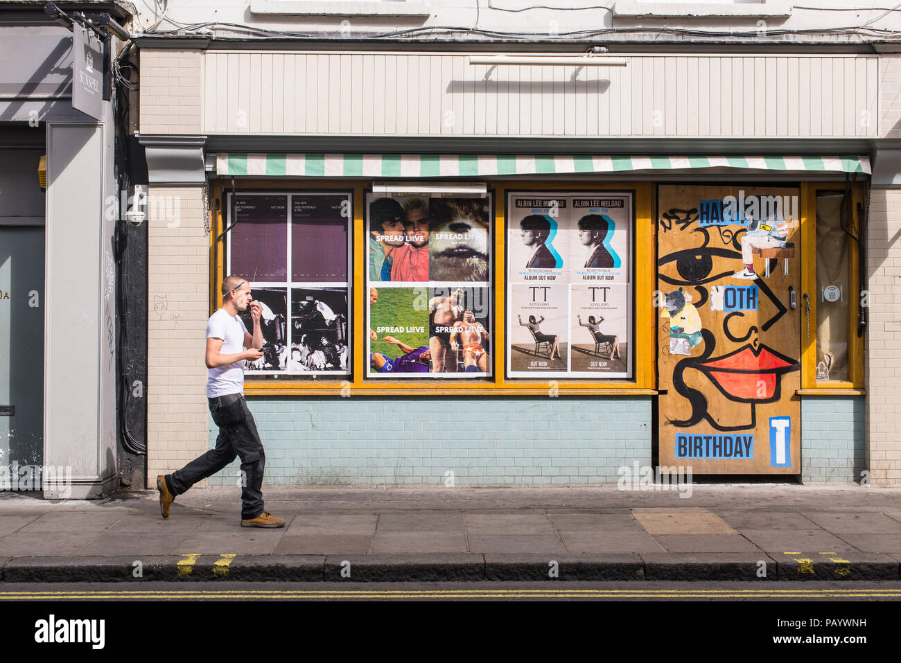 Man Walking in Old Compton Street à Soho en face d'un mur recouvert de panneaux publicitaires et des peintures murales Banque D'Images