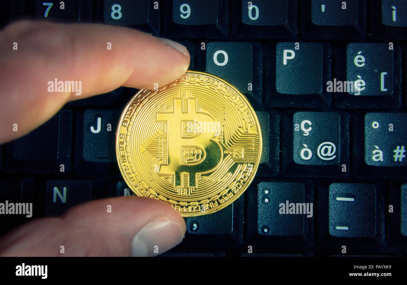 Deux doigts tenant un bitcoin or sur un clavier d'ordinateur. Banque D'Images