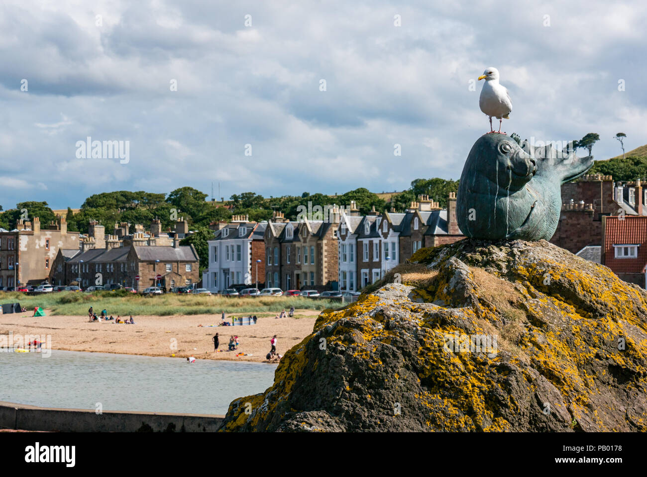 Goéland argenté Larus argentatus sur Joint Sable statue avec Milsey Bay, maisons et mer piscine bassin de baignade, North Berwick, East Lothian, Scotland, UK Banque D'Images