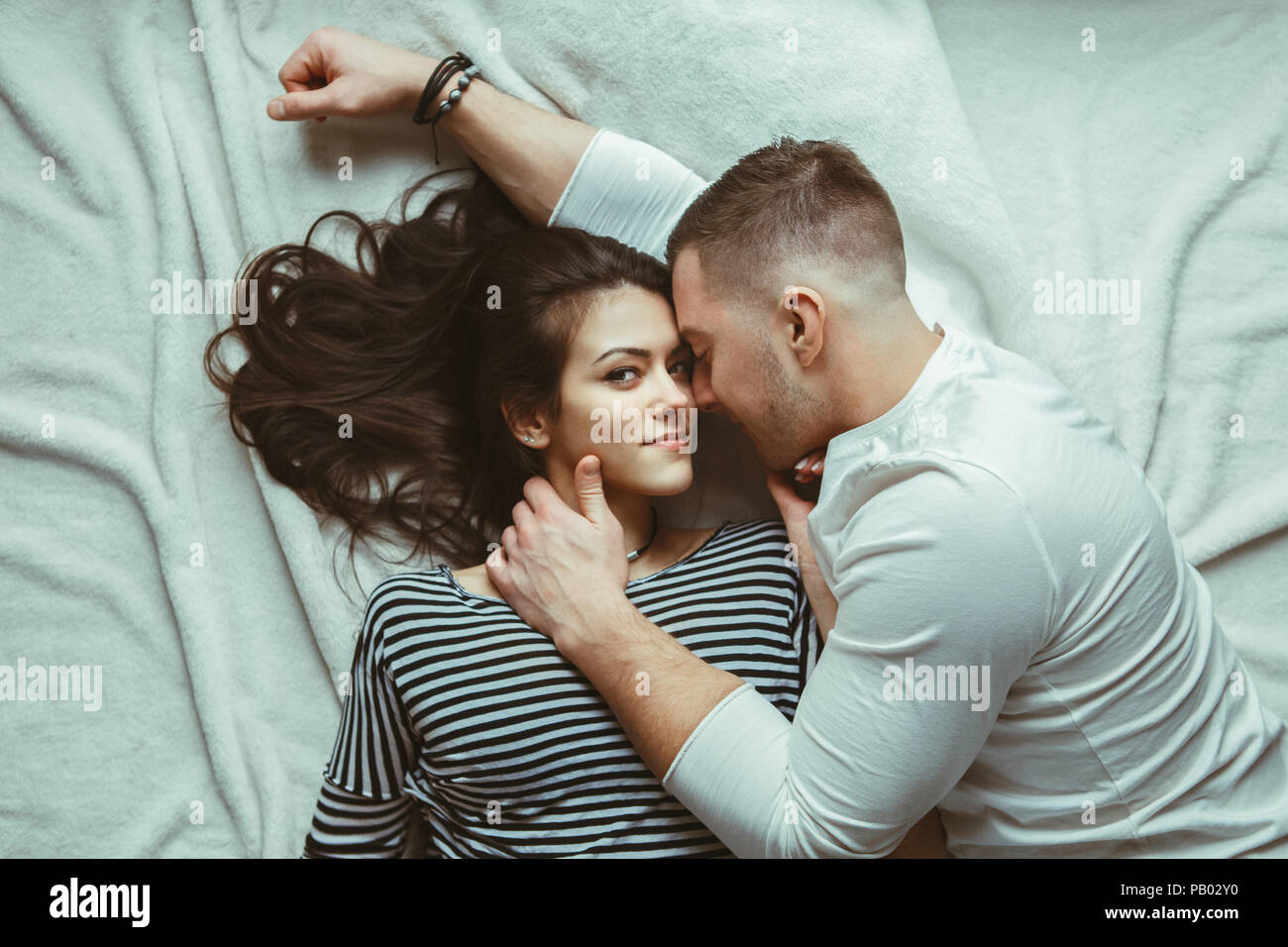 Portrait de beau couple homme femme dans l'amour des caresses, des baisers, couché sur le plancher sur un tapis blanc à l'intérieur de tapis à la maison, tonique avec des filtres Banque D'Images