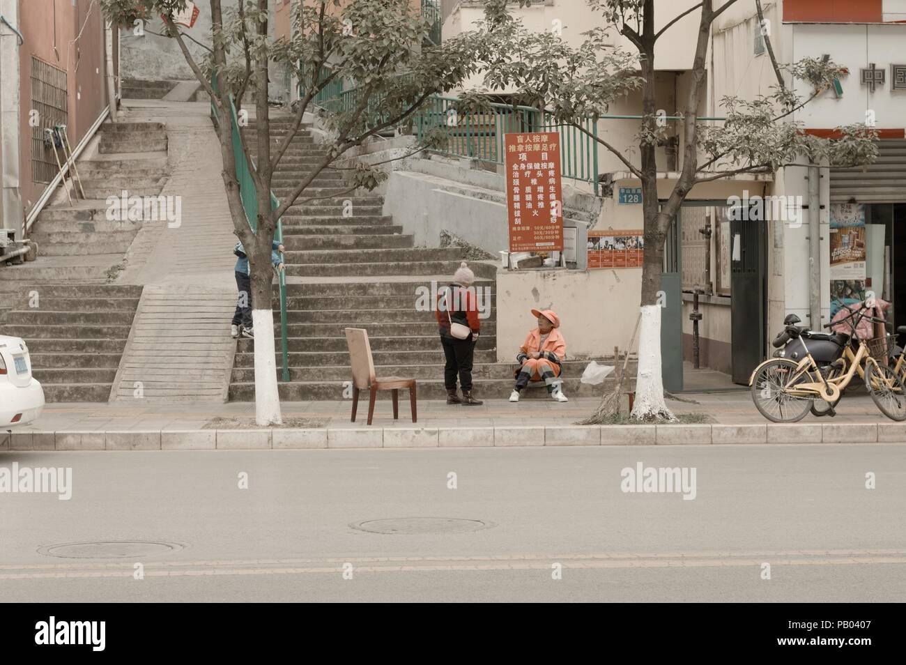 Kunming, Yunnan, Chine - 30 décembre 2017 : deux femmes chinoises sur le trottoir avec une chaise Banque D'Images