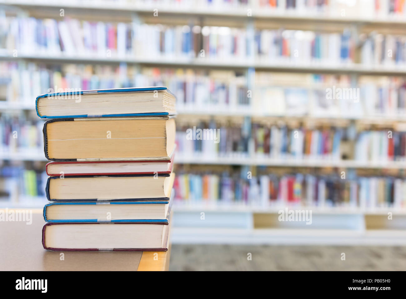 Petite pile de livres de différentes tailles sur bureau bibliothèque avec des étagères de livres derrière Banque D'Images