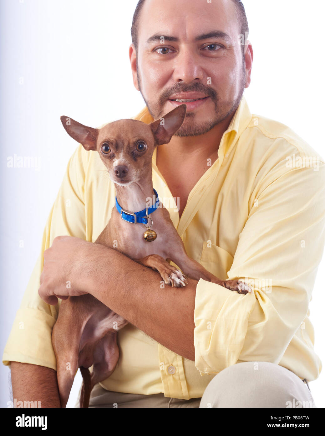 Studio portrait sur un fond blanc d'un homme dans une chemise jaune, tenant un chihuahua chien dans ses bras Banque D'Images