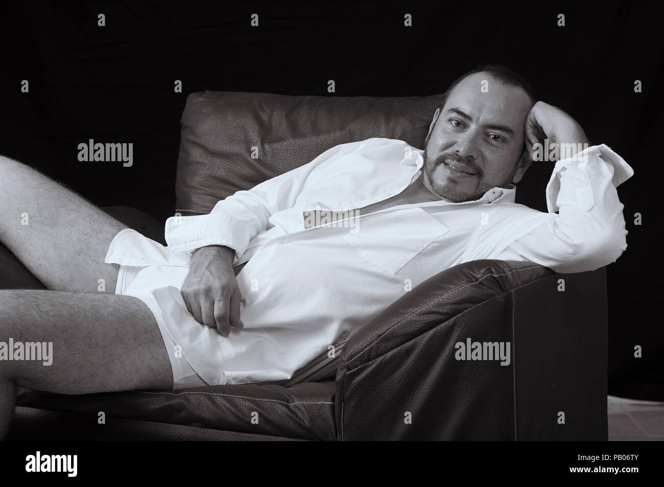 Studio noir et blanc portrait d'un homme en chemise blanche et des mémoires, allongé sur un canapé Banque D'Images
