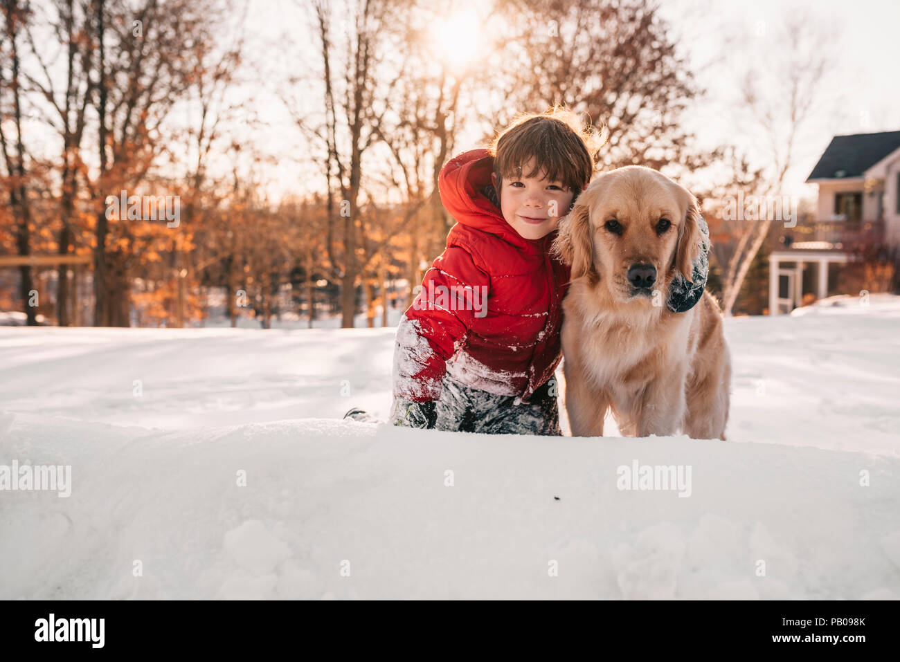 Portrait d'un garçon assis dans la neige avec son chien golden retriever Banque D'Images