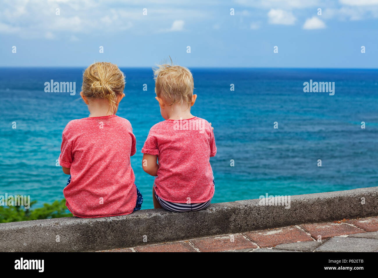 Heureux les enfants s'amuser sur la plage à pied. Couple d'enfants assis sur la falaise, de parler, de regarder et de surf mer ciel bleu. Style de voyage, les activités de plein air en f Banque D'Images