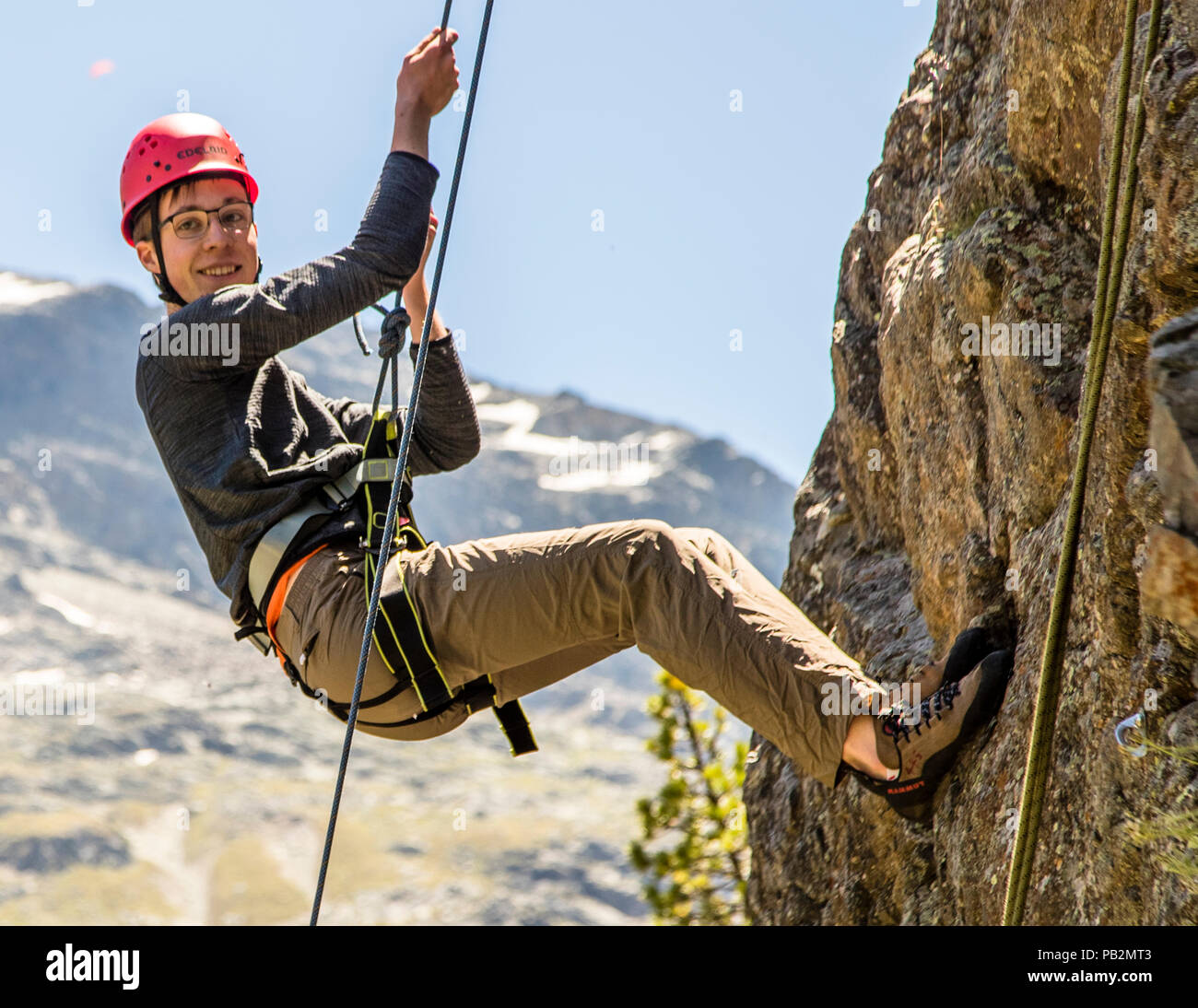 Un jeune homme a enfoncé un rocher en face de Piz Palü. La descente en rappel devant le massif de Piz Palü est la récompense à la fin du cours d'escalade d'introduction. Escalade à Pontresina, Suisse Banque D'Images