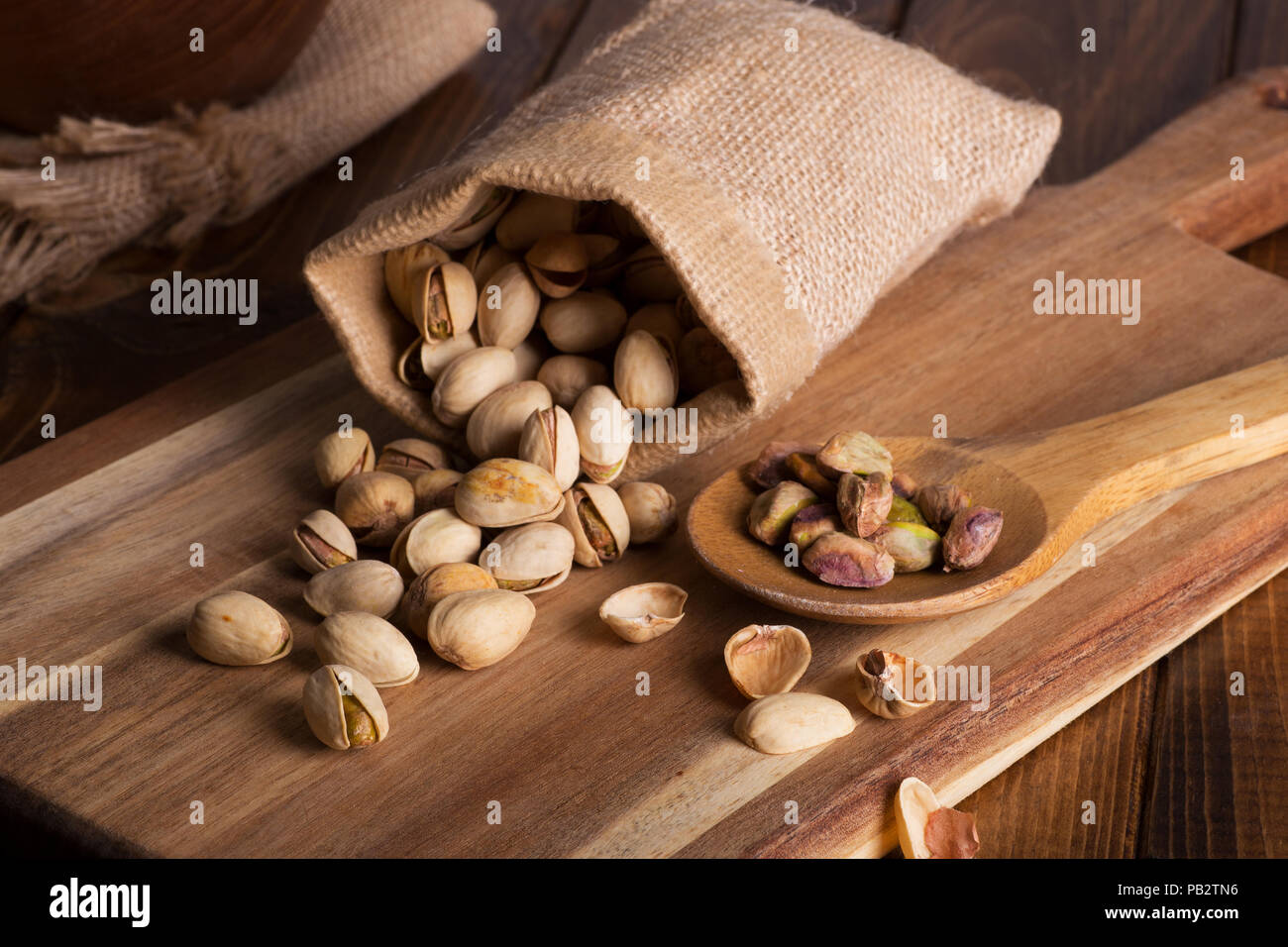 Les pistaches déversés par un sac de toile et une cuillerée de pistaches sur une planche en bois Banque D'Images