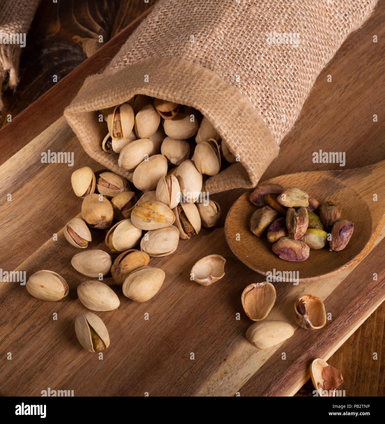 Pistaches déversés par un sac de toile et une cuillerée de noix sur une planche en bois Banque D'Images