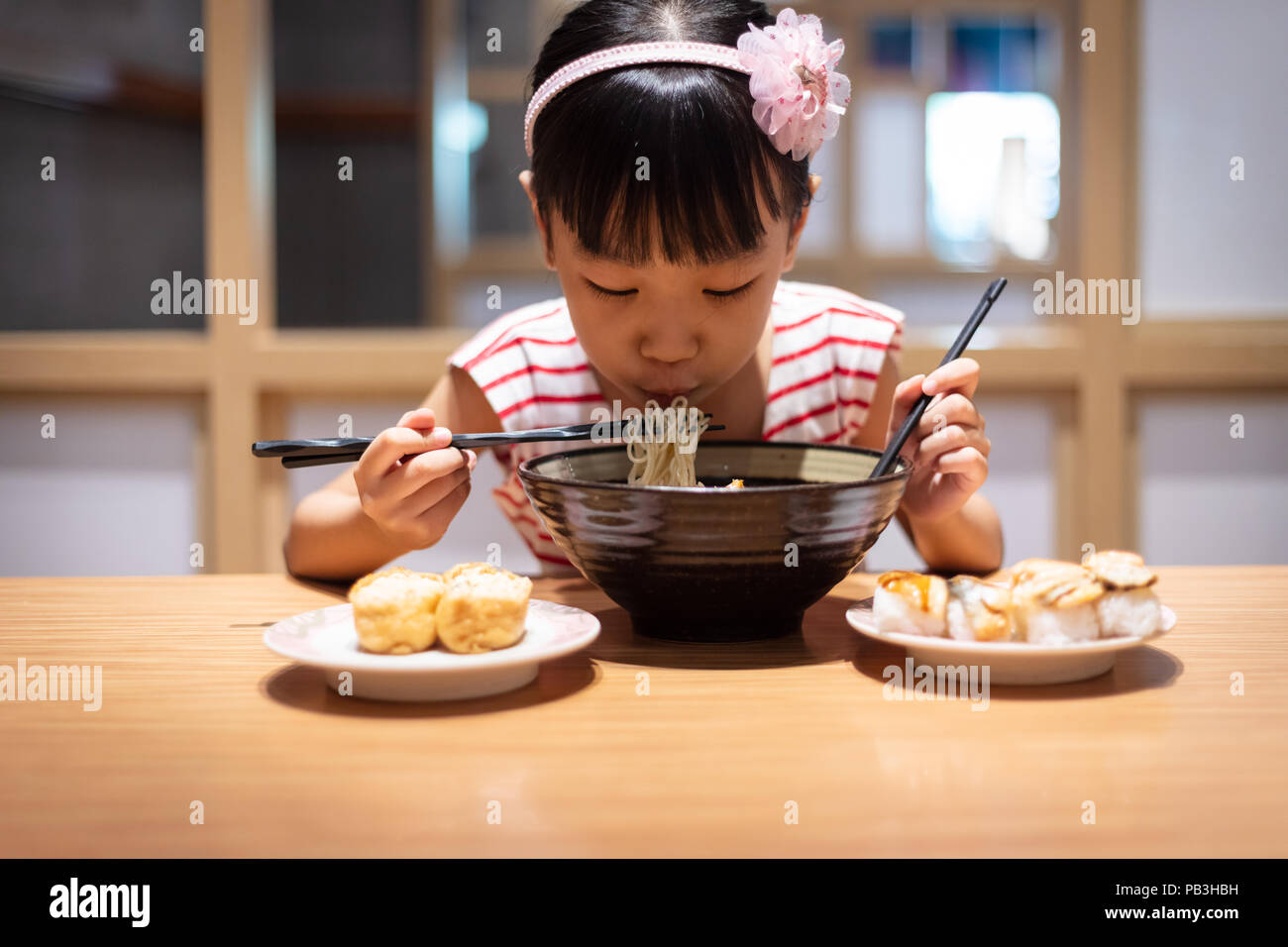 Peu asiatique Chinese girl eating nouilles ramen à un restaurant japonais Banque D'Images