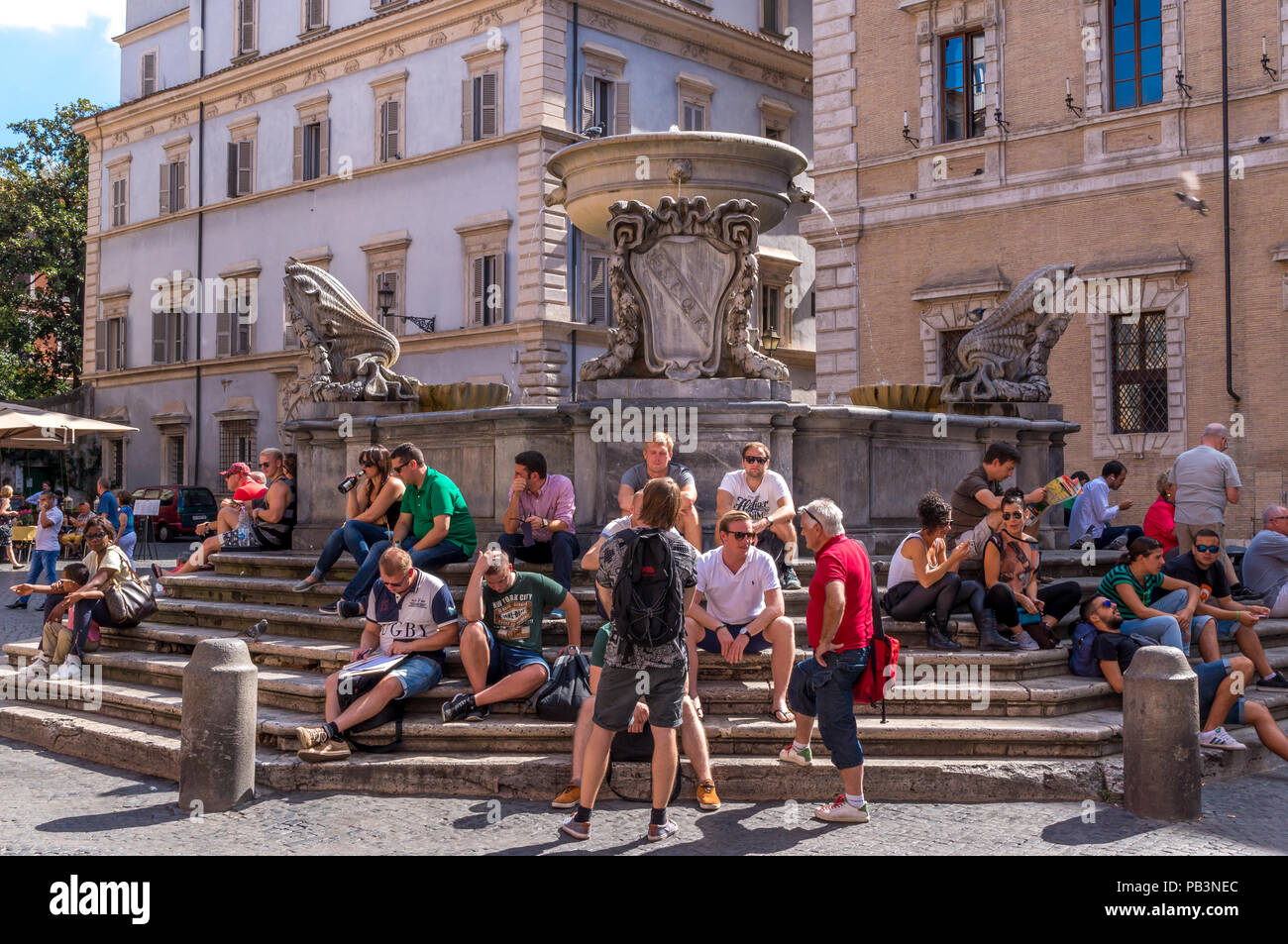 Les jeunes gens assis sur les marches de la fontaine sur la place Santa Maria in Trastevere, Rome Banque D'Images