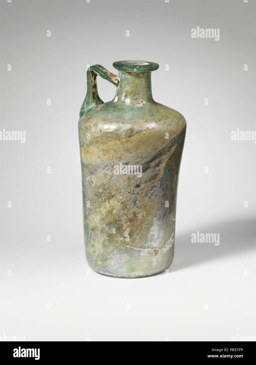 Verseuse cylindrique en verre. Culture : Roman. Dimensions : H. : 5 11/16 in. (14,4 cm). Date : 1re, 3e siècle de notre ère. Vert, bleu translucide avec poignée de même couleur. Rim déployée, et, depuis, avec la surface supérieure aplatie et les lèvres autour de la bouche ; l'expansion du cou vers le bas ; épaule oblique vers l'extérieur avec bord arrondi ; corps cylindrique légèrement avec le côté concave diminuant progressivement vers le bas ; fond concave ; trois nervures poignée sangle attachée à l'épaule, établi à la verticale, puis se tourna à un angle aigu et traînées sur le cou. Intacts ; peu de bulles ; ternissement, de légères piqûres, irisés, et de petites parcelles de la météo Banque D'Images