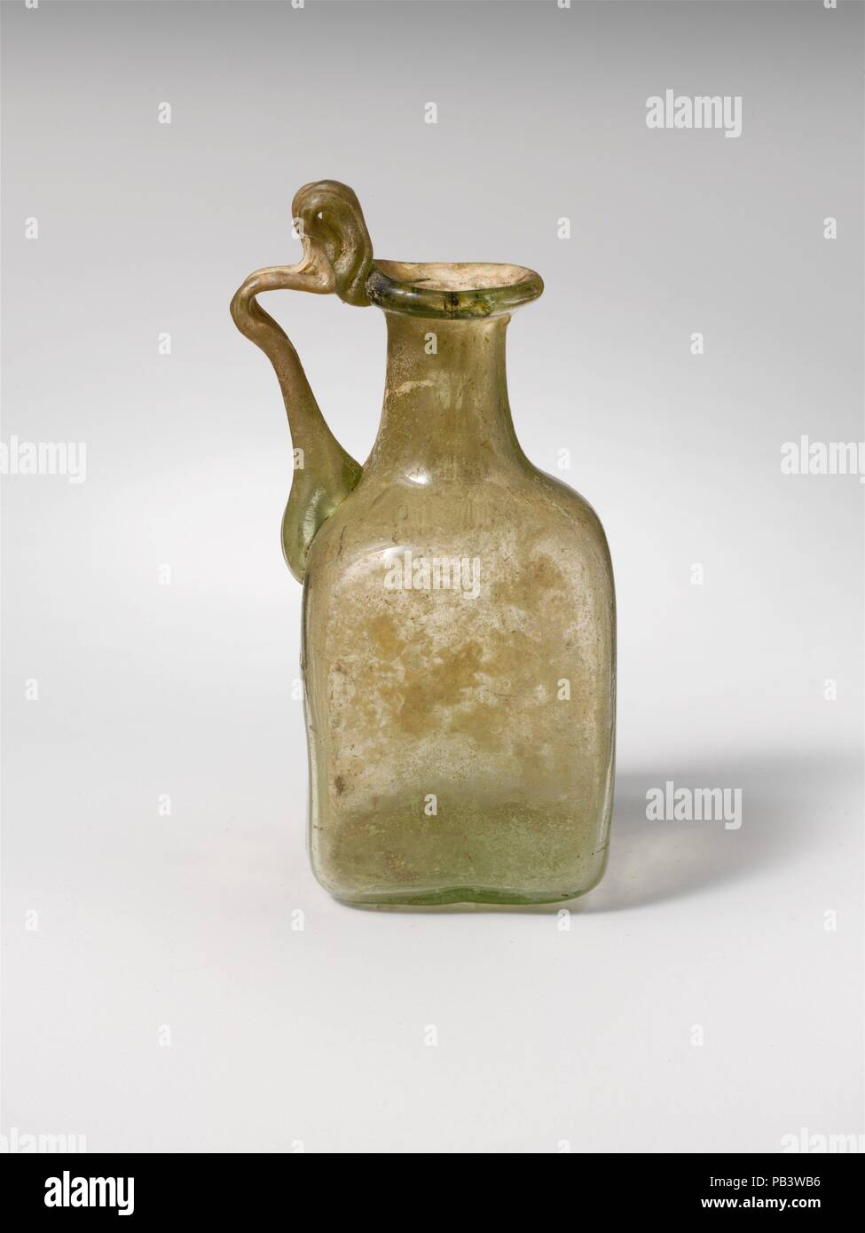 Bouteille en verre. Culture : Roman. Dimensions : hors tout : 3 x 5/16 1 7/16 x 1 7/16 in. (8,4 x 3,7 x 3,7 cm) Diam. : 7/8 in. (2,2 cm). Date : 1re, 3e siècle de notre ère. Les petits traités flacon carré. Jaune Vert translucide ; poignée de même couleur. Rim dépliées, ronde, et dans, et pressé dans d'autre de la bouche, du cou cylindrique, l'extension vers le bas ; oblique ; corps carré avec des côtés inégaux et arrondie coins inférieurs ; fond plat ; deux poignée striée est attaché à l'épaule, établis à l'extérieur, tourné à l'horizontale, et traînées sur le bord extérieur de la jante avec la boucle ci-dessus. D'un côté, modèle resem soulevé Banque D'Images