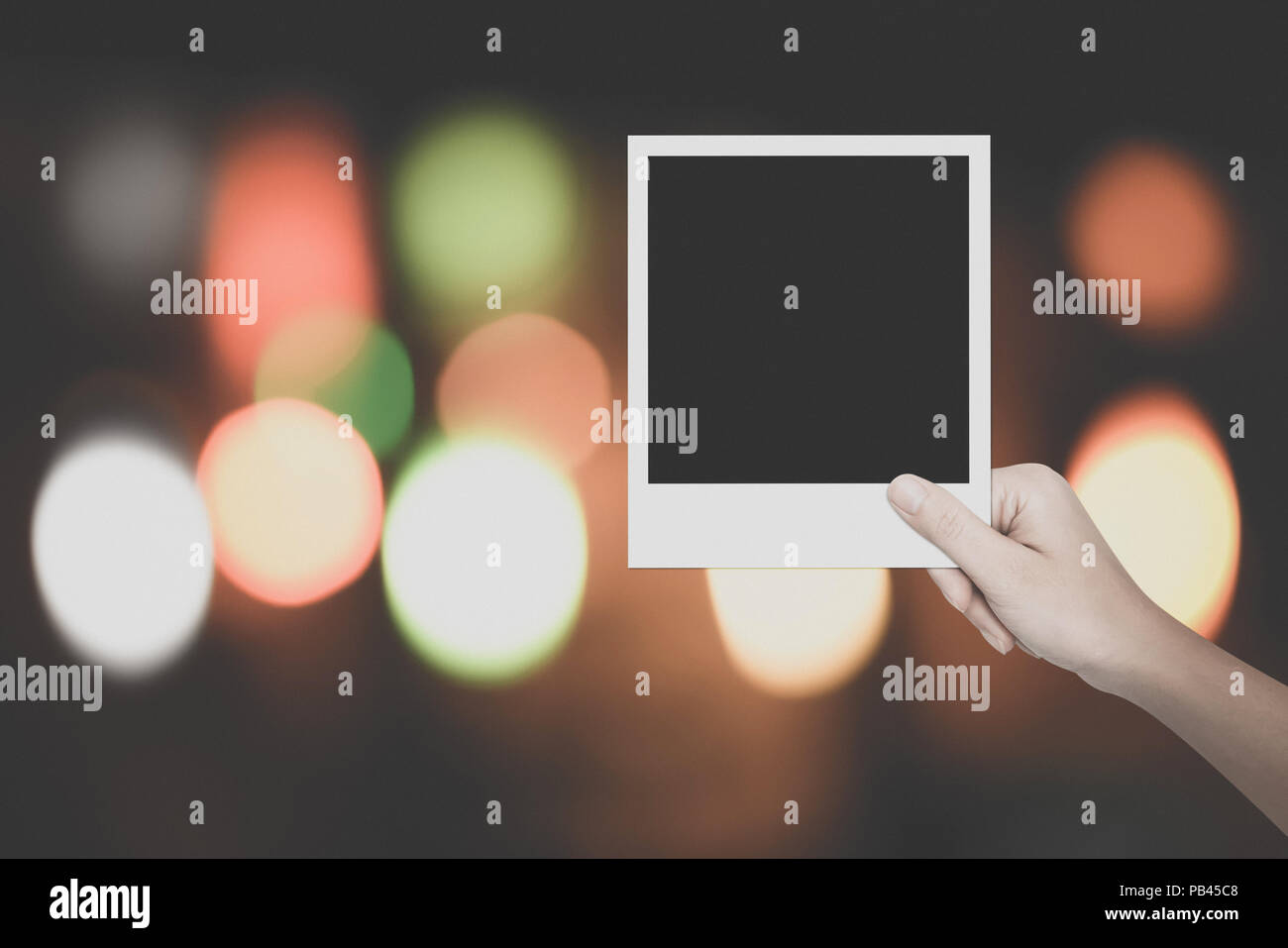 Main de Femme tenant un cadre photo Blanc sur fond coloré effet bokeh - vintage style Banque D'Images