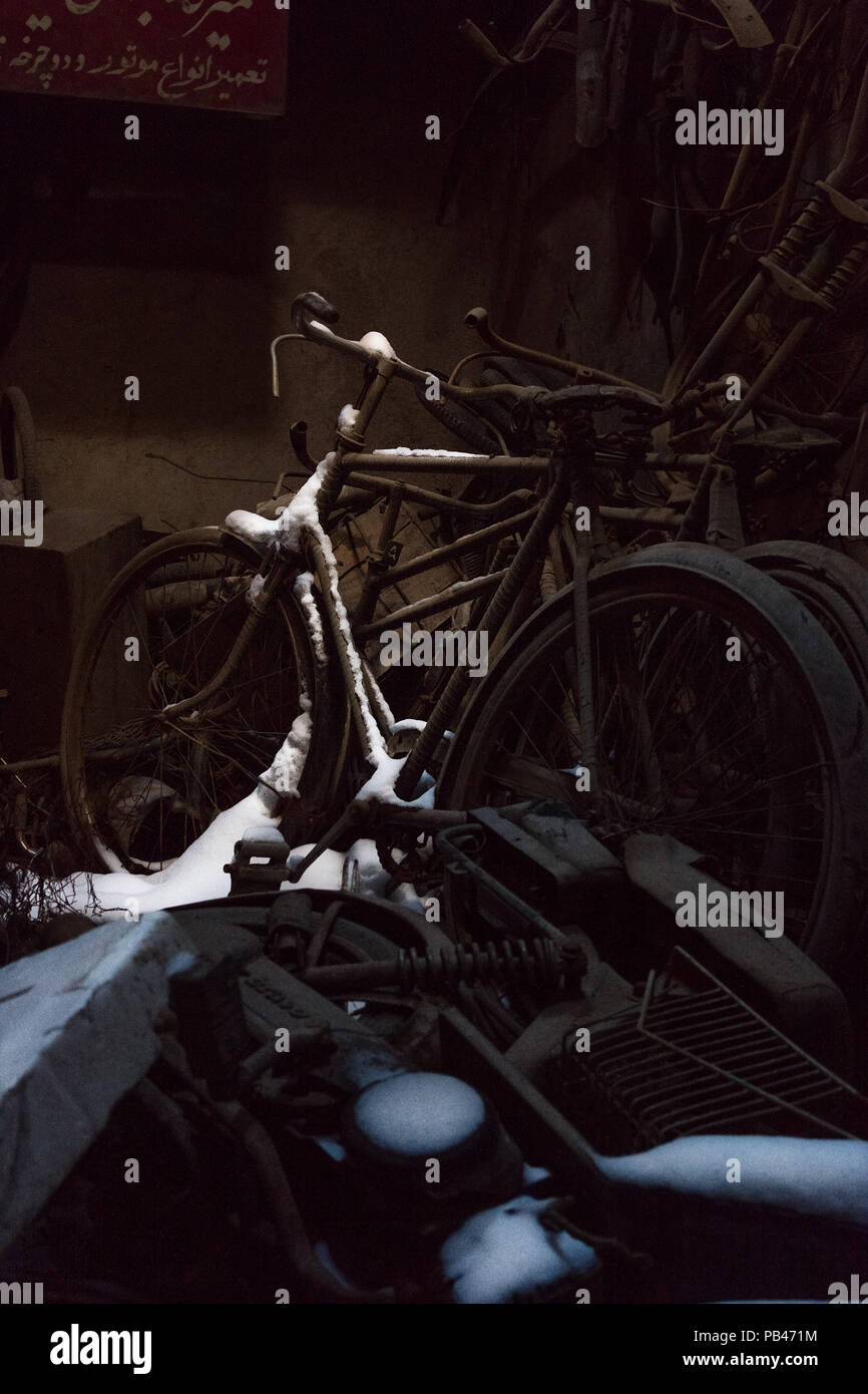 Vieux vélos rouillés et une moto sont abandonnés dans un ancien atelier de réparation avec une couverture de neige qui est tombé à travers un trou dans le toit. Banque D'Images