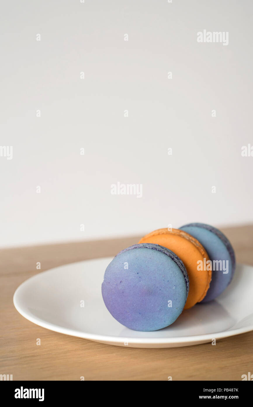 Trois Macarons Orange et bleu assis sur leurs côtés sur une plaque - verticale Banque D'Images
