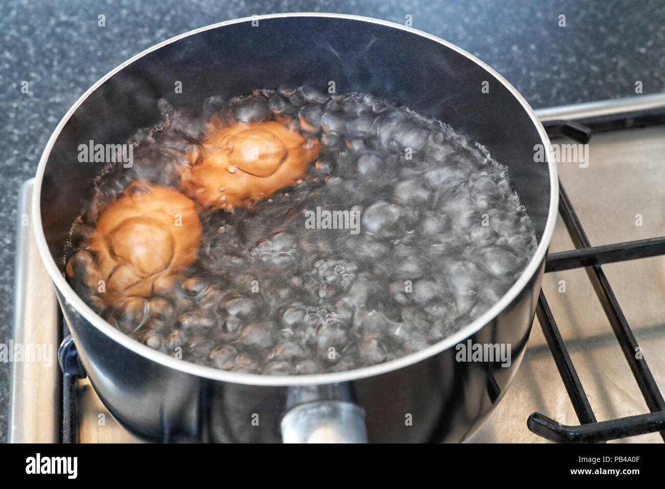 Deux œufs à l'ébullition dans une casserole sur une cuisinière à gaz / cuisinière Banque D'Images
