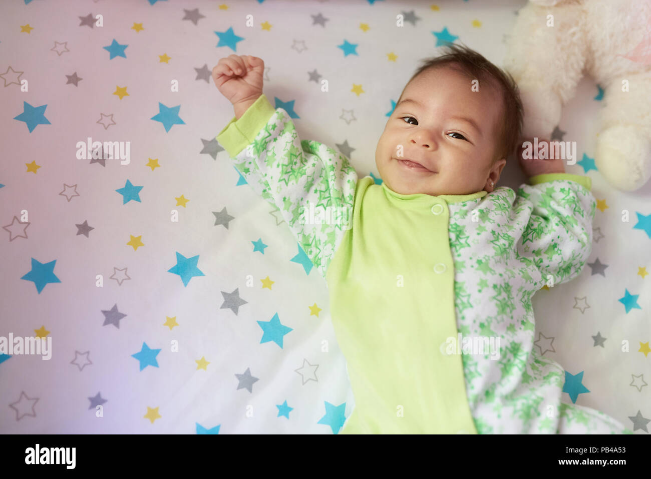 Happy baby girl laying on bed with hands up Banque D'Images