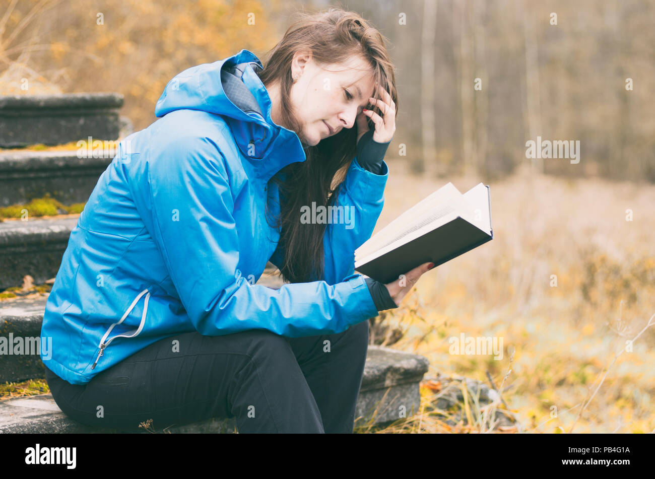 Fille ébouriffa ses cheveux en pensée tout en lisant un livre sur l'historique de la forêt d'automne et le feuillage jaune. Film stylisée. Banque D'Images