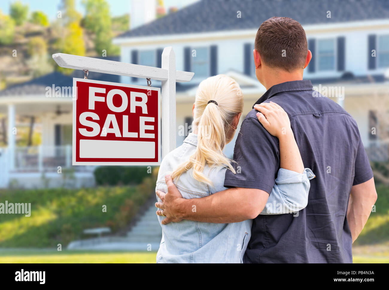 Young Adult couple face à l'avant du Achat Immobilier signe et maison. Banque D'Images