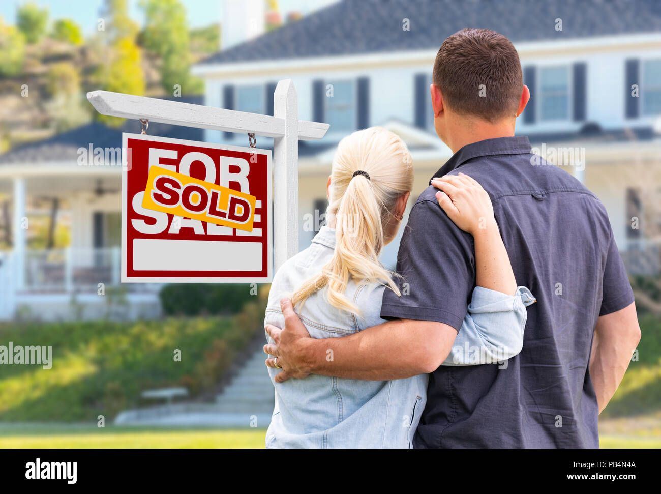 Young Adult couple face à l'avant du vendu enseigne immobilière et de la Chambre. Banque D'Images