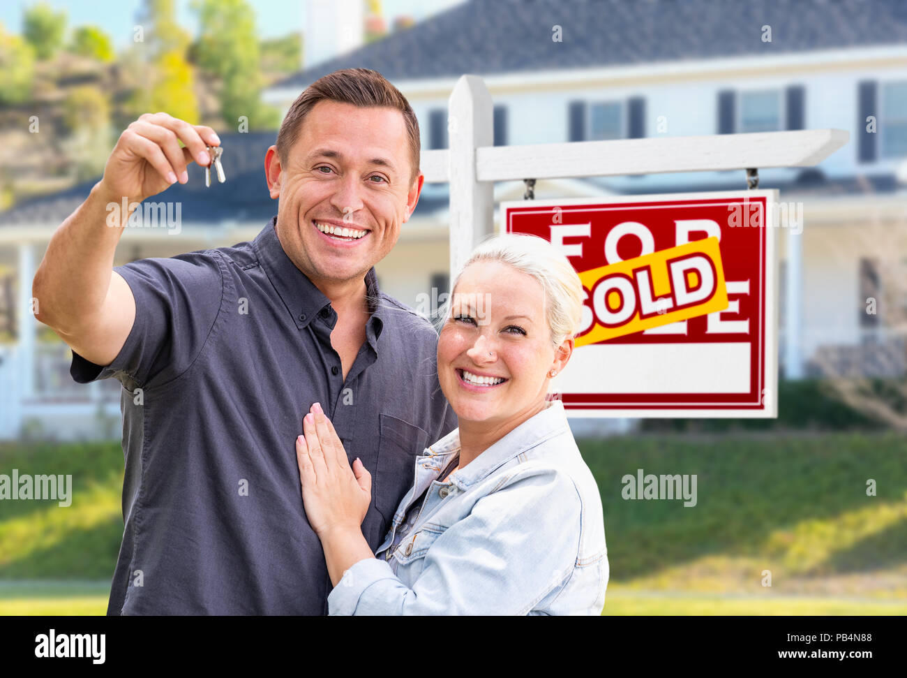 Jeunes adultes en couple avec clés de maison en face de la maison et vendu à la vente enseigne immobilière. Banque D'Images