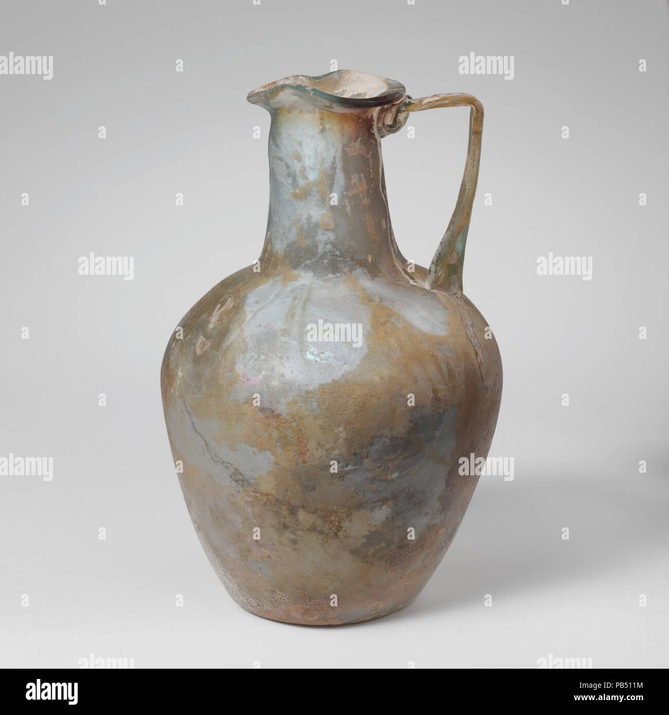 Verseuse en verre. Culture : Roman. Dimensions : hors tout : 5 3/4''. (14.6cm) Autres : 3. en 11/16 (9,4Cm). Date : Mi-1er et 2e siècle de notre ère. Bleu vert translucide ; poignée et sentier dans la même couleur, le violet streak dans la jante et le cou. Bord arrondi éversée, estampé en forme de trèfle, ovale, en forme d'entonnoir du cou ; oblique ; corps effilé vers le bas avec côtés convexes ; fond concave ; poignée sangle avec trois côtes appliquée à l'épaule, établis à l'extérieur, tourné dans horizontalement pour RIM, et traînées sur l'en haut du col et le dessous de la jante. Complète, mais les fissures dans le haut du corps au-dessous de la poignée, fonctionnant jusqu'à l'épaule et du cou r Banque D'Images