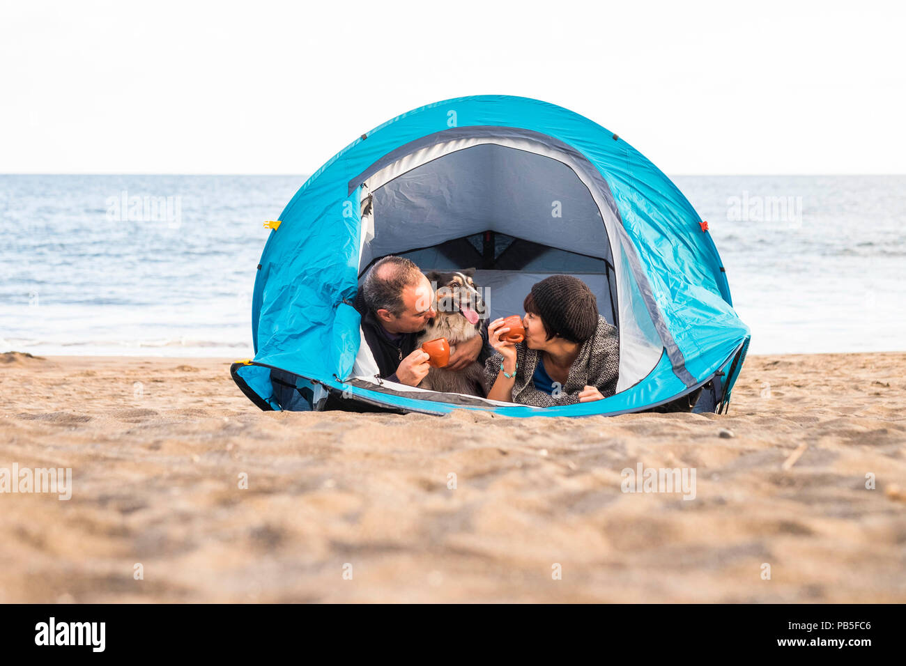 Couple le téléphone intelligent et avoir du plaisir à l'intérieur d'une tente dans un camping sur la plage chien border collie derrière eux regardant la caméra. Banque D'Images