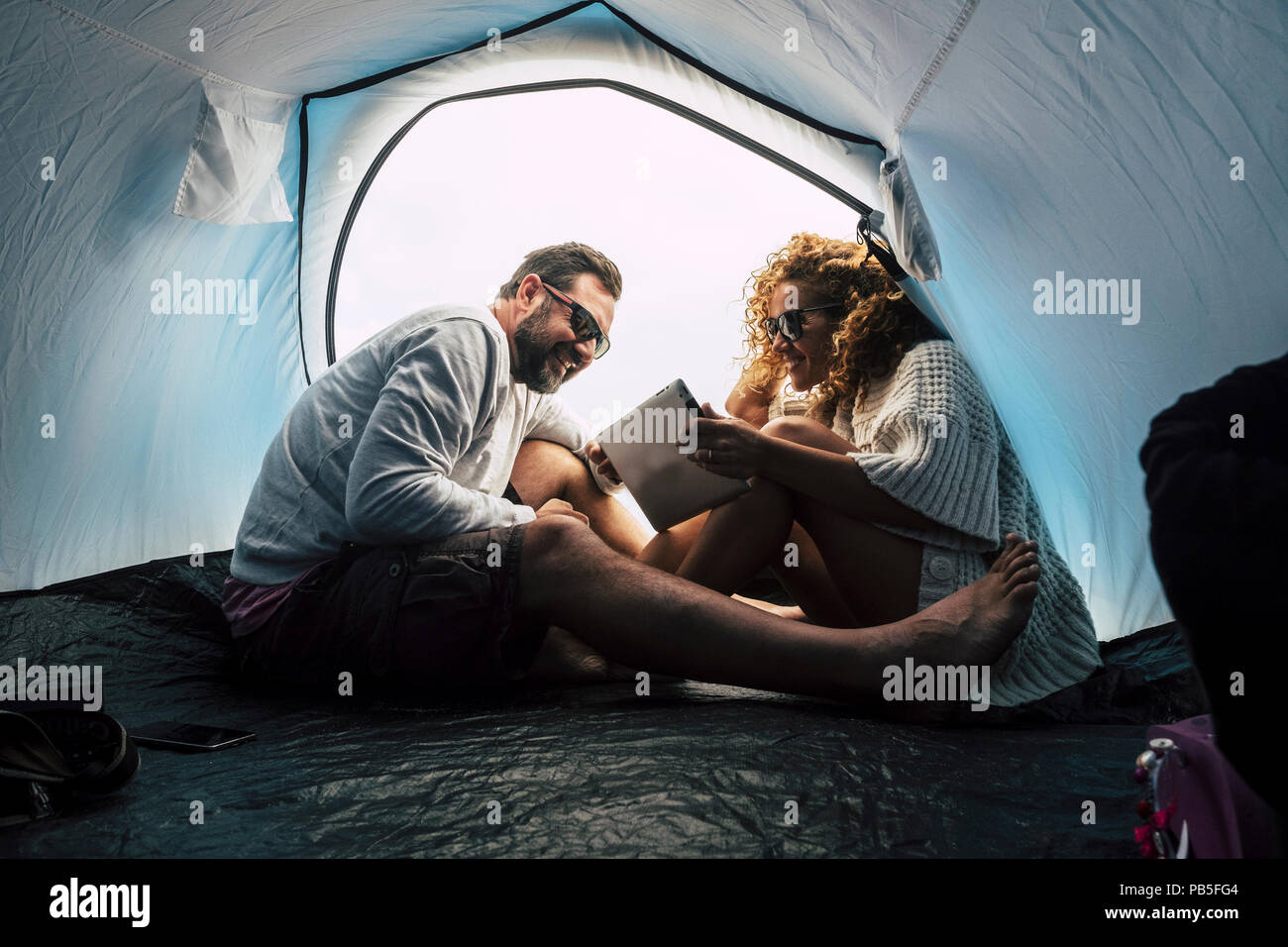 Happy young couple d'âge moyen et mariés dans la relation à l'intérieur de la tente de camping et de l'utilisation de la technologie internet tablet. L'amour et l'amitié fo Banque D'Images