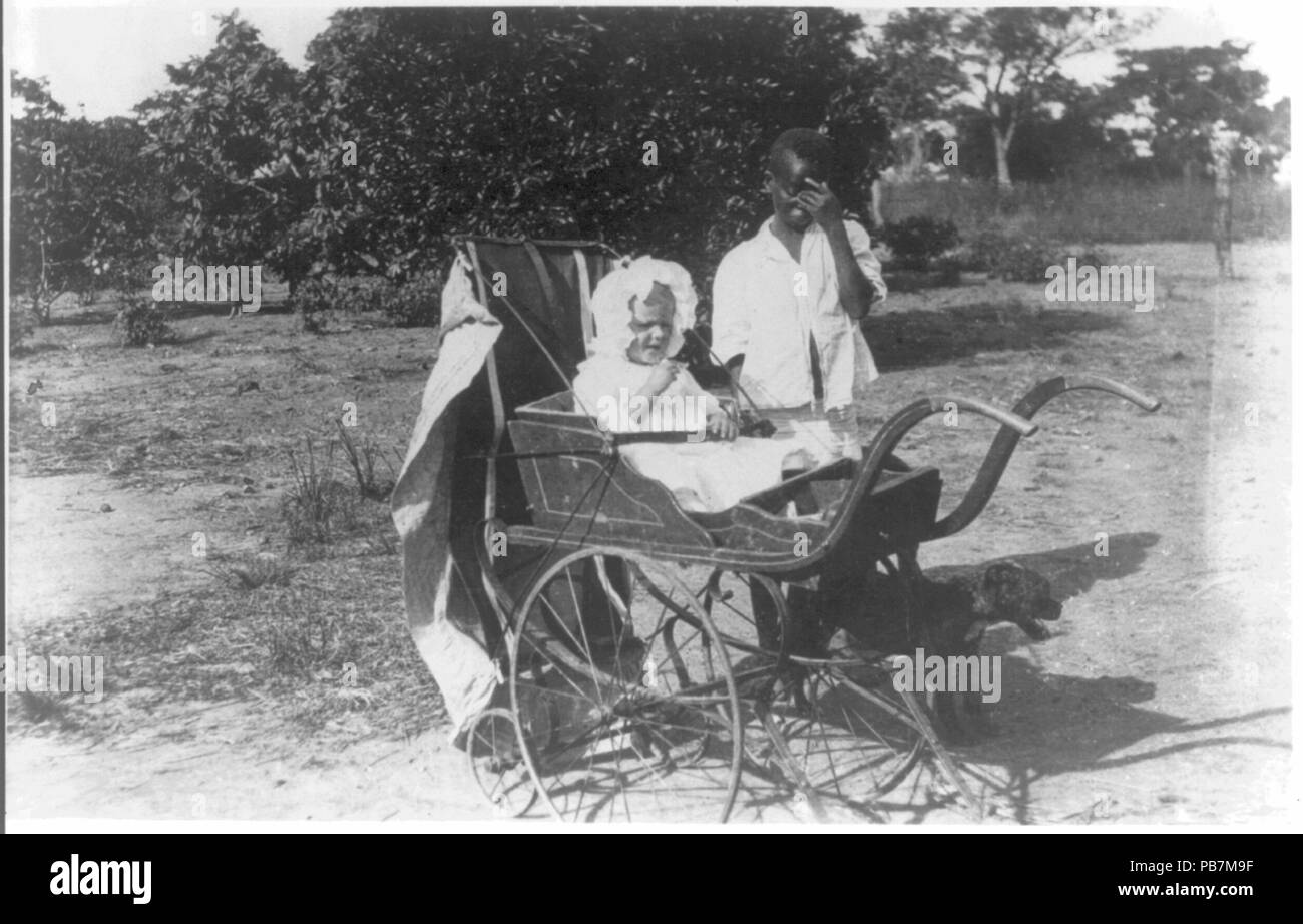 1850 enfant blanc dans baby carriage assisté par garçon noir. L'Afrique. ca. 1924. Rcac2001705527 Banque D'Images