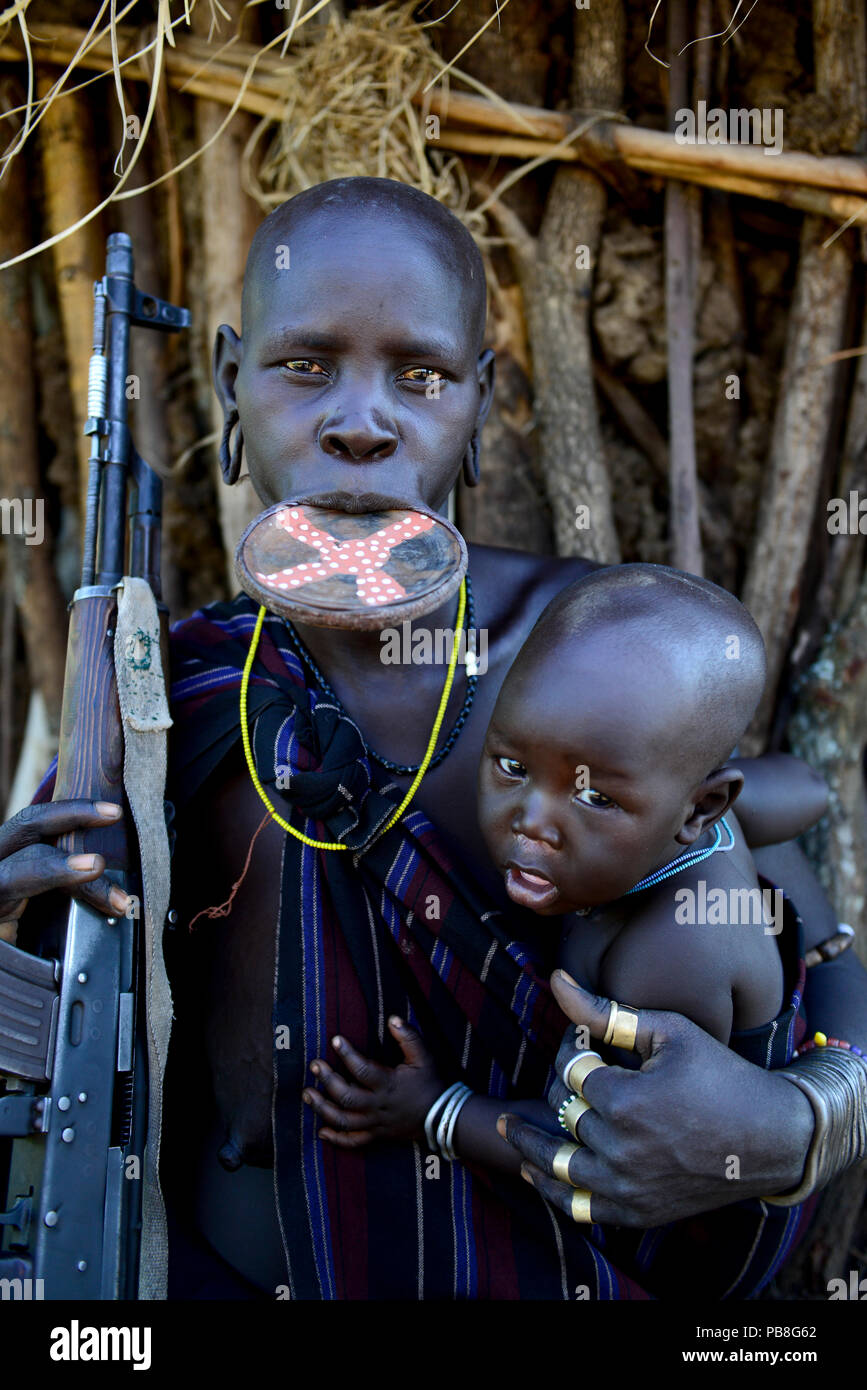 Femme Mursi avec lèvre d'argile, de la plaque et son fils. carabine holding Mago Parc National. Vallée de l'Omo, en Ethiopie. Banque D'Images