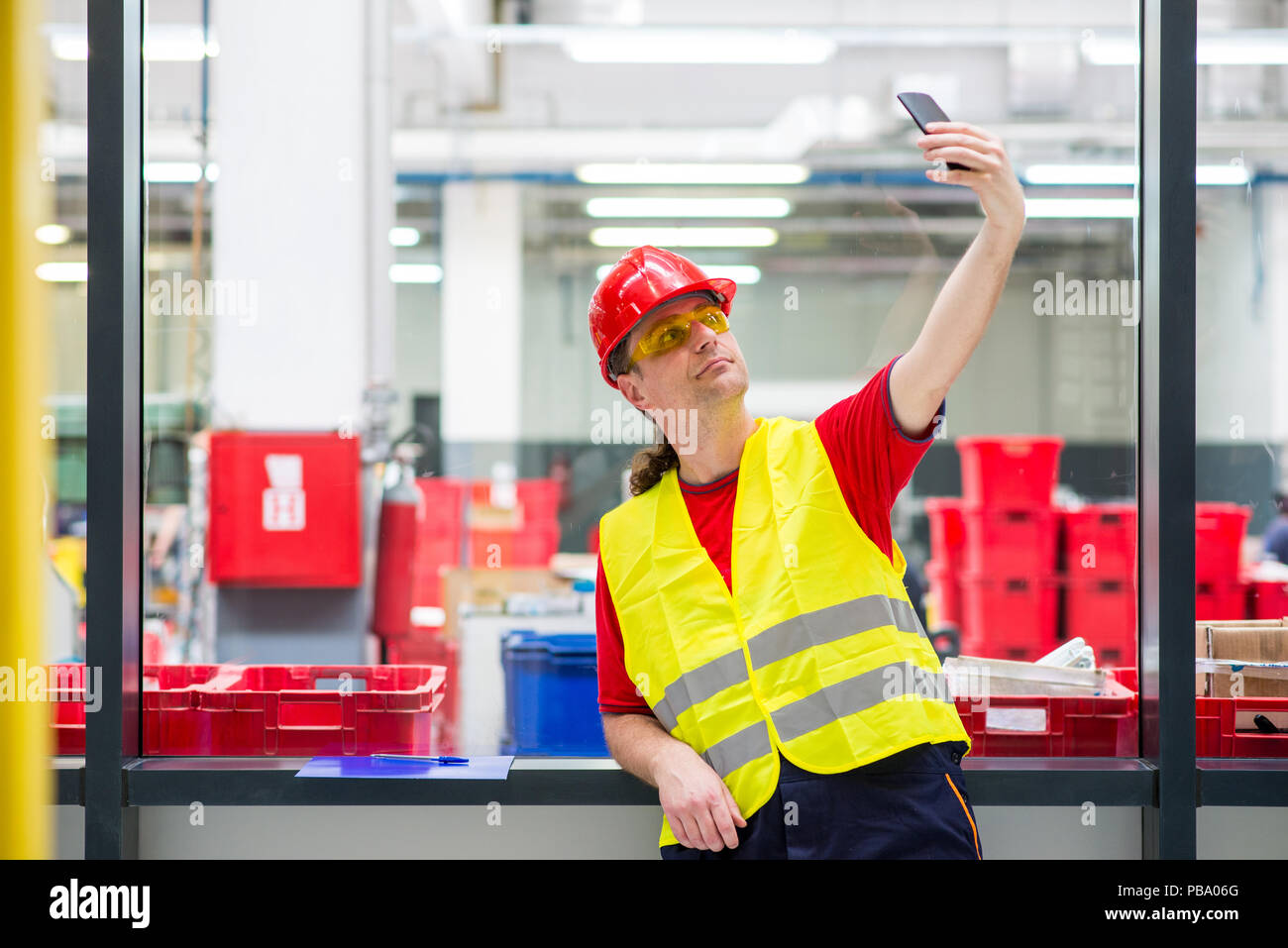 Travailleur de l'usine en tenant son téléphone portable avec selfies dans l'usine Banque D'Images