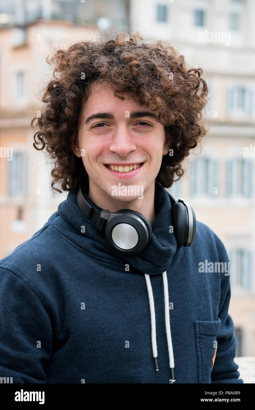 Portrait de beau jeune homme avec les cheveux bouclés avec des écouteurs autour de son cou Banque D'Images