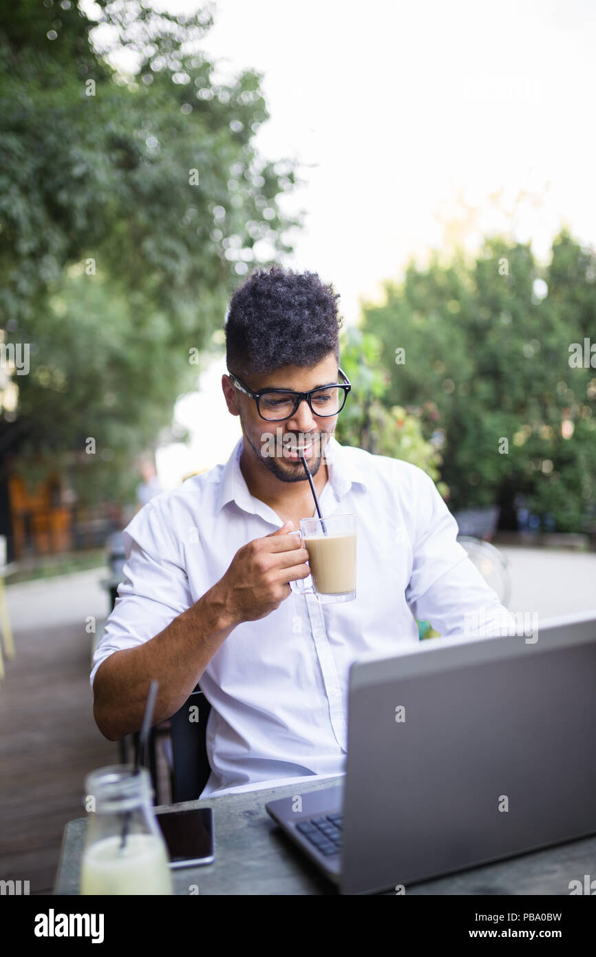 Les jeunes afro-américains attractive businessman sitting in cafe bar, boire du café et avoir fait quelques travaux sur ordinateur portable. Banque D'Images