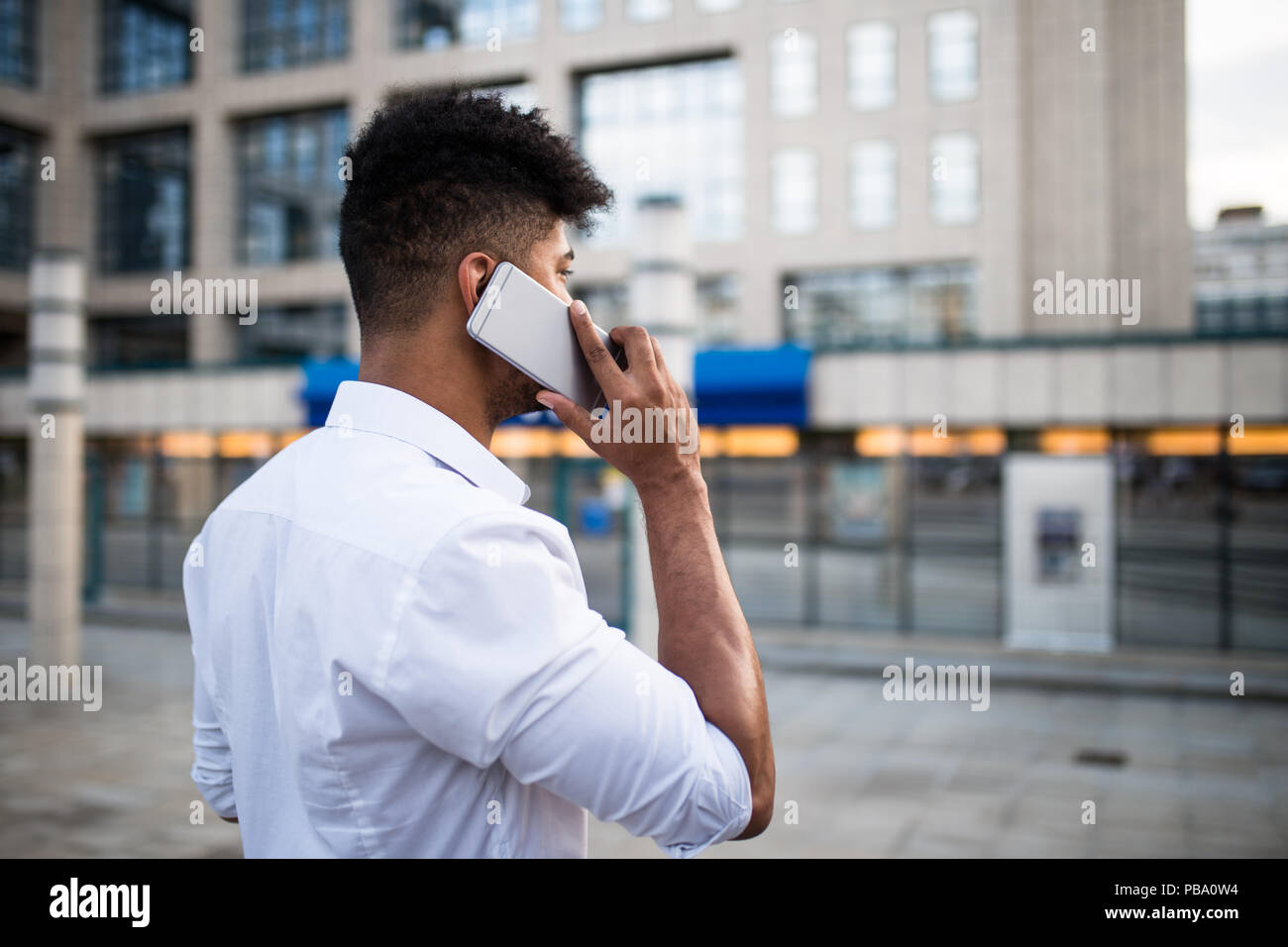 Beau jeune homme afro-américain debout devant d'énormes capacités d'affaires moderne ; sourire et parler sur téléphone mobile. Banque D'Images