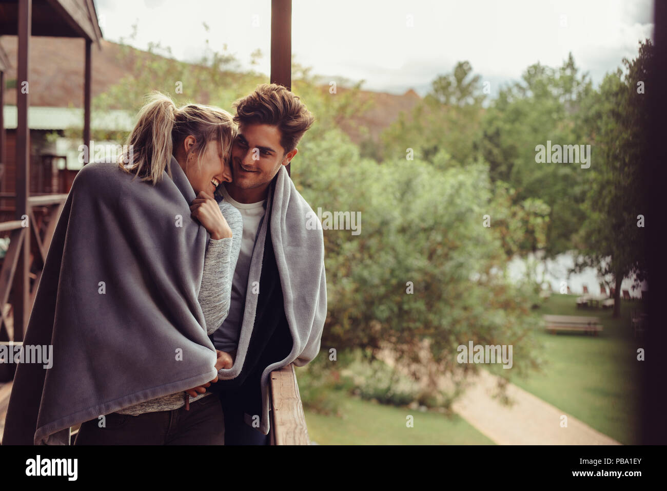 Aimer l'homme et la femme debout dans leur chambre d'hôtel balcon enveloppé dans une couverture. Couple romantique dans une couverture debout ensemble sur des vacances d'hiver. Banque D'Images