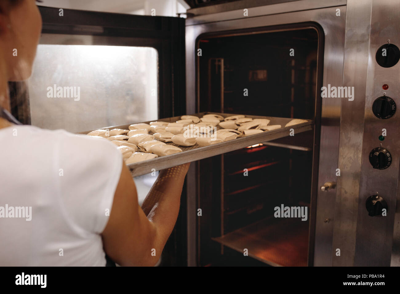 Mettre une femelle baker cuisson plein de bobines de four. Woman baking rouleaux dans une boulangerie. Banque D'Images
