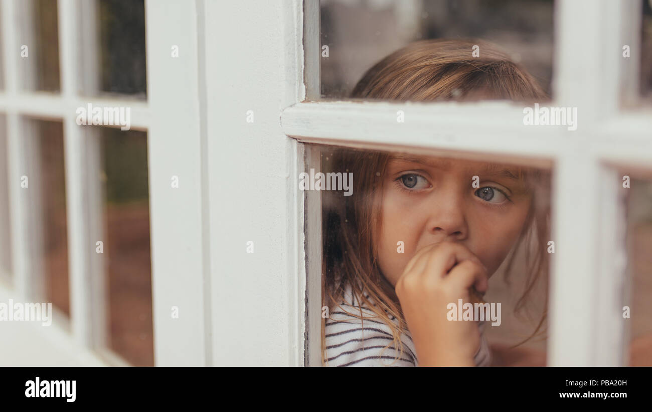 Gros plan d'une petite fille assise à côté d'une fenêtre et à l'extérieur. Gray eyed girl eating un gâteau tout en regardant par la fenêtre. Banque D'Images