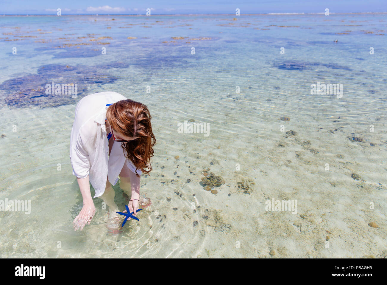L'ile Des Femmes De La Mer La femme trouve l'étoile de mer bleue sur la côte de corail des Îles
