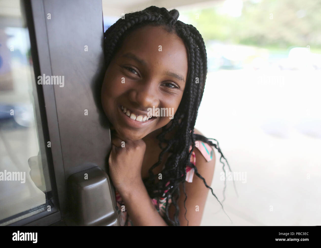 Dix ans African American girl sourit et ouvre la porte de l'école. Banque D'Images