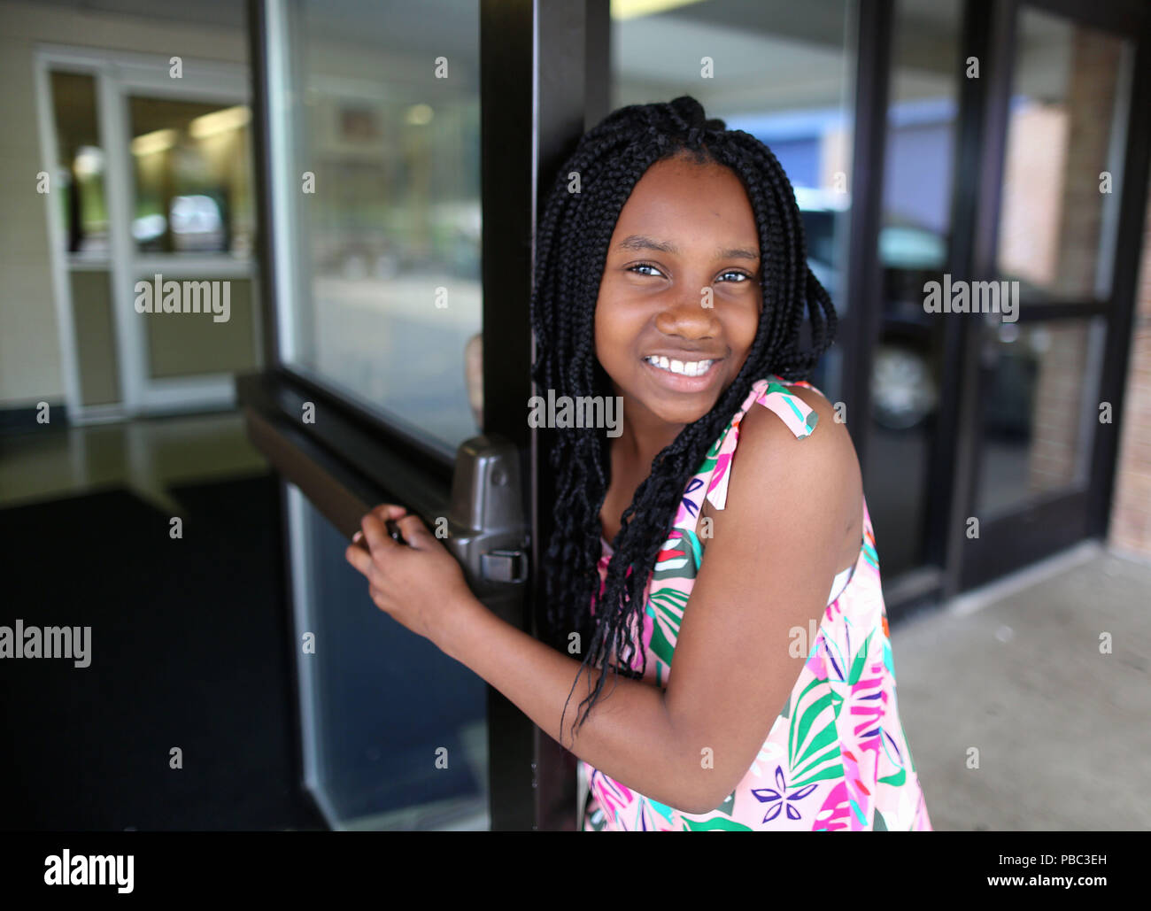 Dix ans African American girl sourit et ouvre la porte de l'école. Banque D'Images