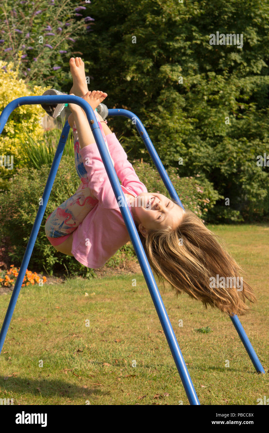 Fillette de six ans faire des acrobaties sur appareil de gymnastique dans le jardin arrière pour jouer, au Royaume-Uni. Banque D'Images