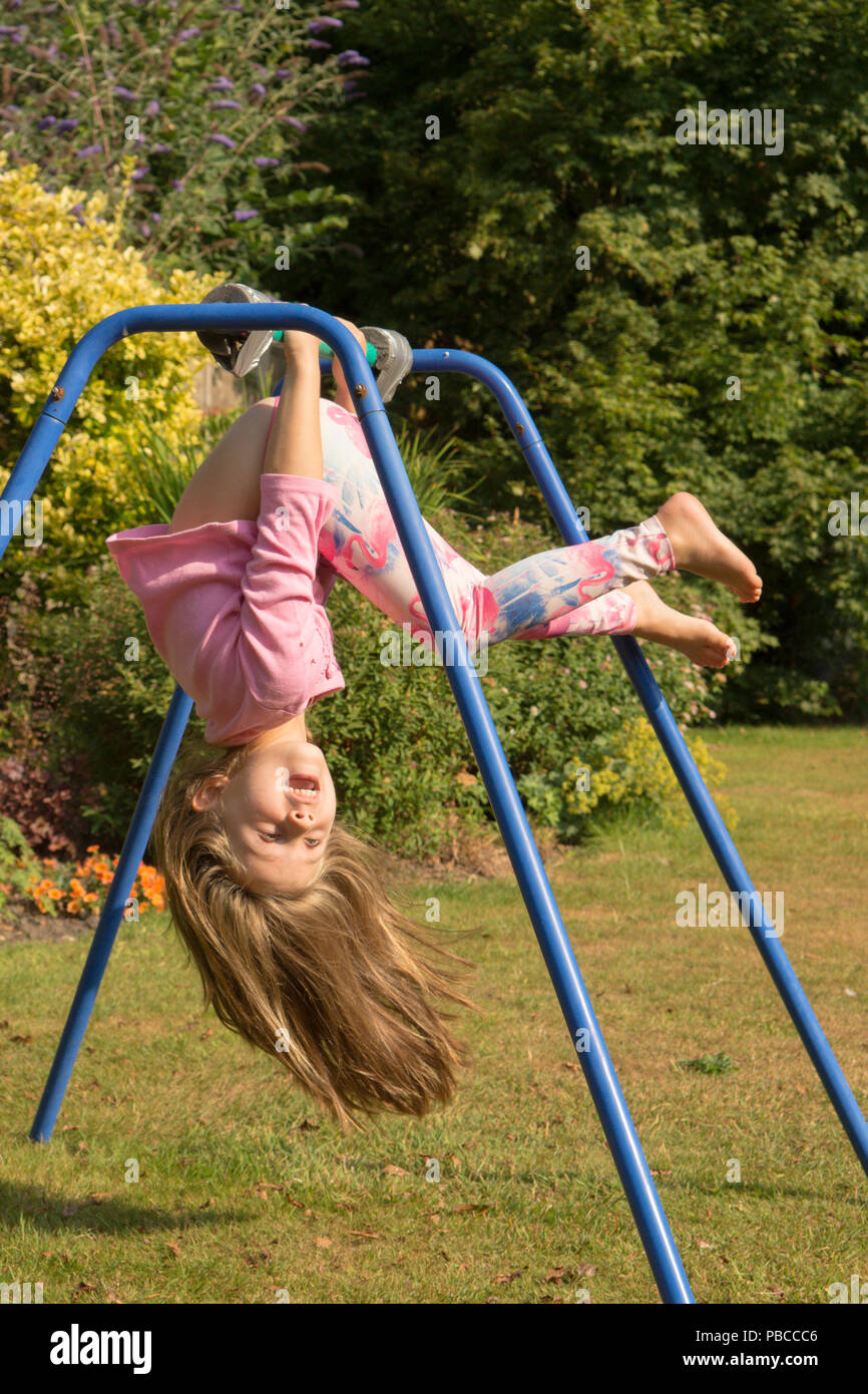 Fillette de six ans faire des acrobaties sur appareil de gymnastique dans le jardin arrière pour jouer, au Royaume-Uni. Banque D'Images