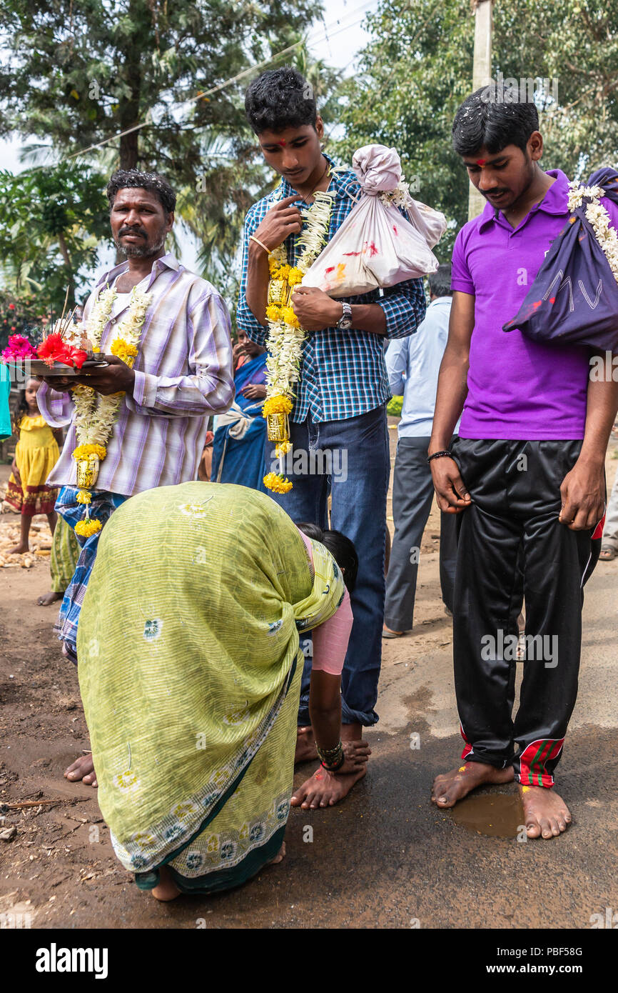 Belathur, Karnataka, Inde - 1 novembre, 2013 : Pilgrim d'hommes et se laver les pieds par femme pendant la cérémonie d'adieu. Guirlandes, sacs à dos, et beaucoup de couleurs Banque D'Images