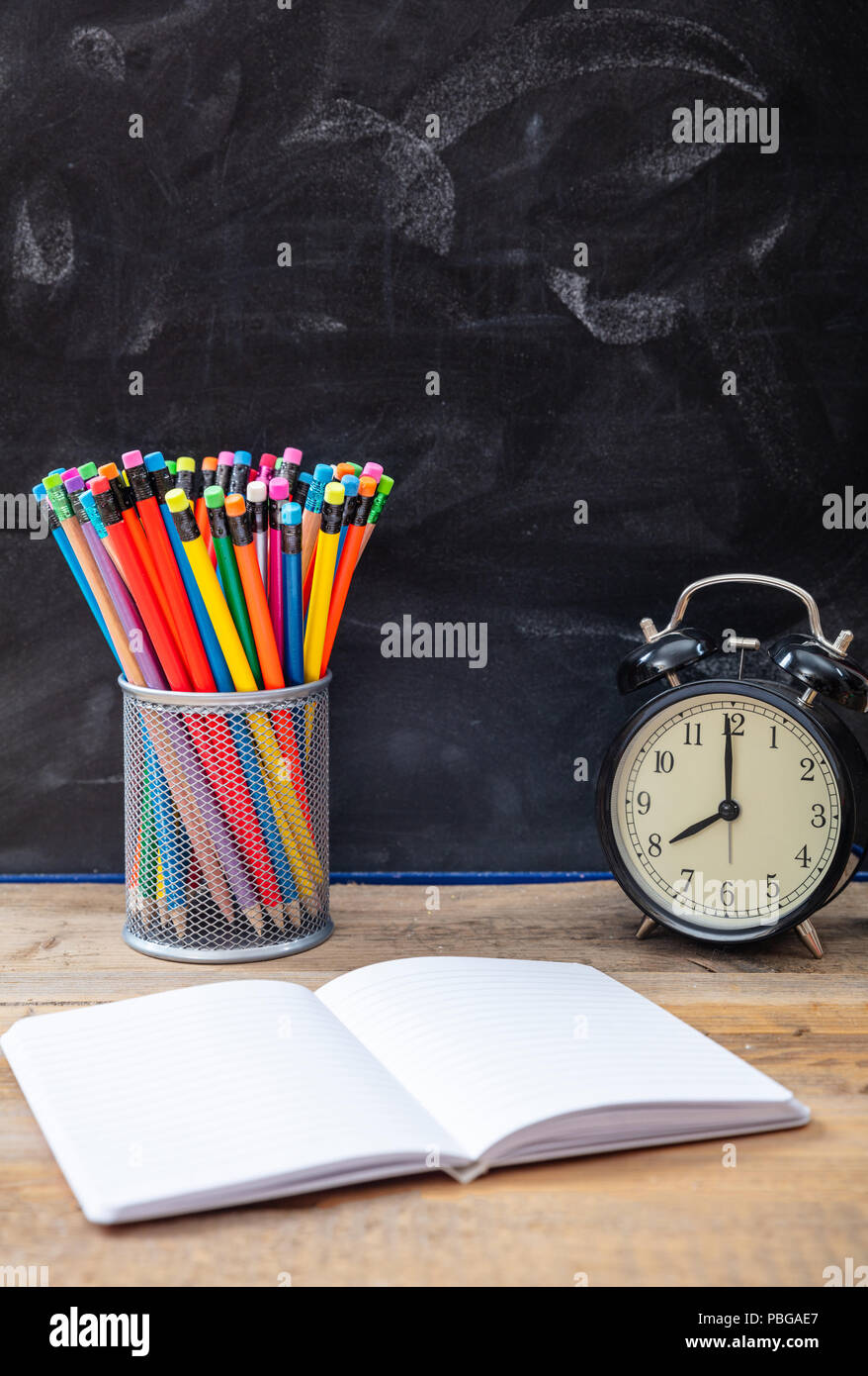 De temps pour l'école. Les fournitures scolaires et réveil sur un bureau en bois, blackboard background Banque D'Images