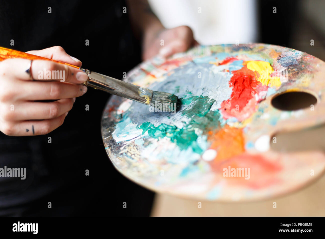 Femme artiste créatif de noir holding brush et derrière la palette chevalet dans studio près de la fenêtre Banque D'Images